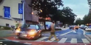 Mężczyzna przechodzi przez przejście dla pieszych przed samochodem osobowym na ulicy w mieście o zmierzchu.